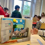 Photographie avec en premier plan une maquette et à l'arrière quelques élèves.